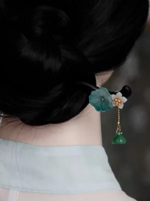 Woman wearing a traditional Chinese hair stick secured in a neat black bun with the lotus pendant hanging over a light cyan Hanfu collar