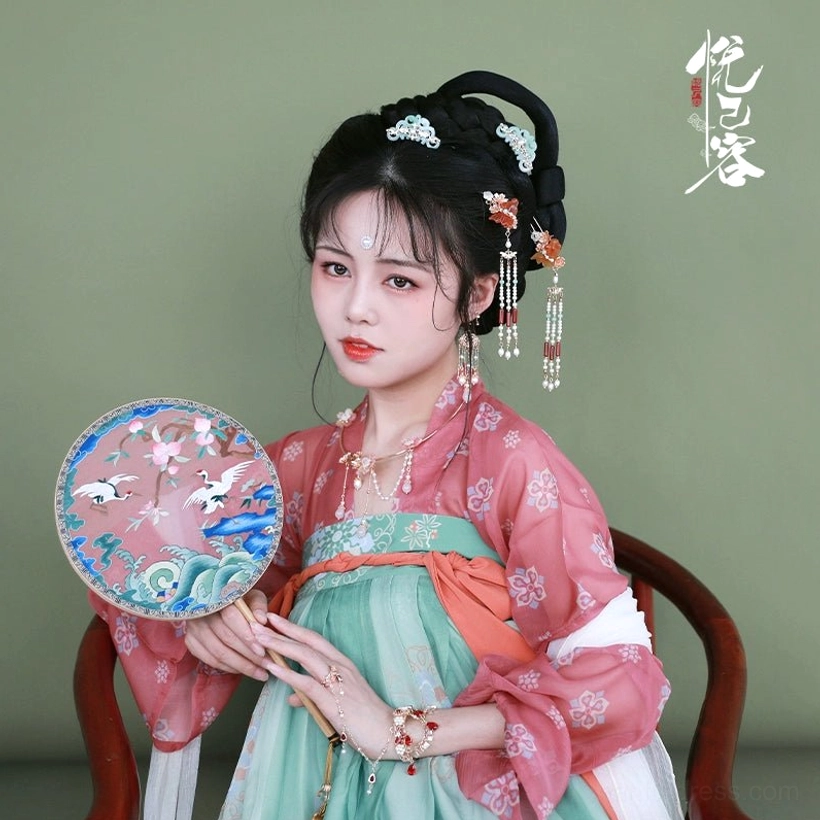 Woman wearing an ornate Chinese Hanfu tassel hair pin with a floral Tang-style Hanfu outfit and holding a traditional Chinese hand fan