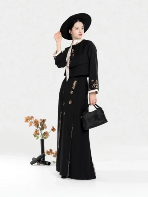 Side-front view of a women's black embroidered Hanfu set with golden floral details, cropped Chinese-style jacket, long pleated skirt, black hat, and handbag
