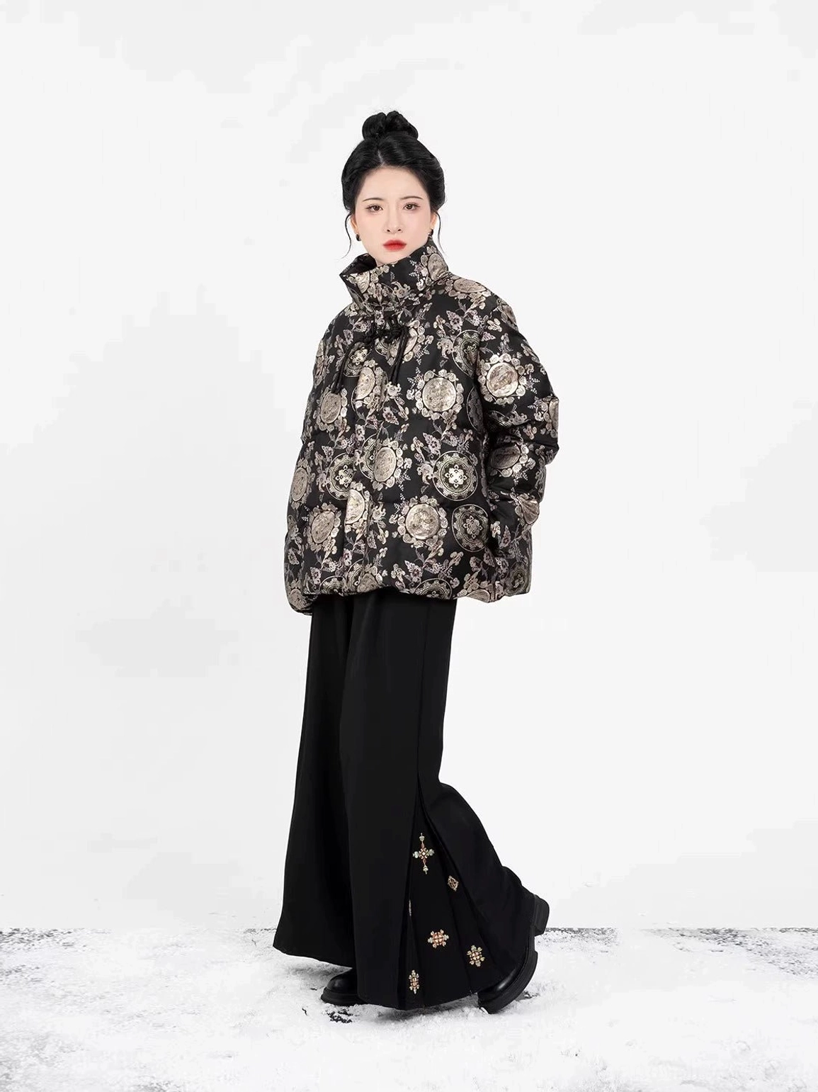 Full-body styling of a women's black and gold Chinese-style floral jacquard puffer coat paired with high-waisted black wide-leg trousers