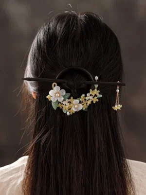 Woman wearing a wooden osmanthus Hanfu hair pin with white flowers yellow blossoms green leaves and pearl tassel in a traditional updo