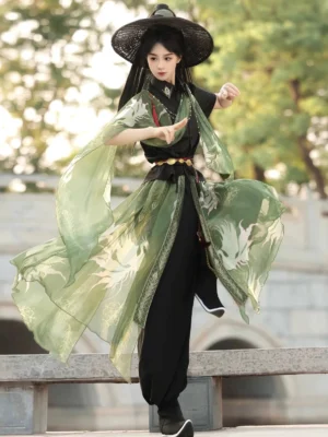 Front three-quarter view of a black and green wuxia-inspired modern Hanfu outfit with flowing printed scarves, decorative waist details, and red tassel accents in a traditional Chinese garden
