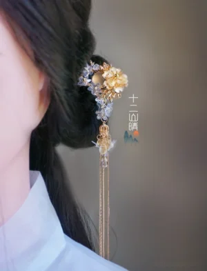Side view of Xiangling Chinese gold floral tassel hair pin worn in a bun with light blue Hanfu outfit