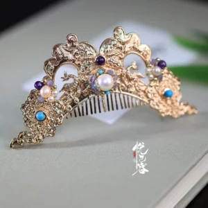 Intricate Xiangsi Hanfu hair crown with carved dragon and phoenix inspired relief patterns, pearl details, colorful stone accents, and vintage golden metal finish displayed on a book