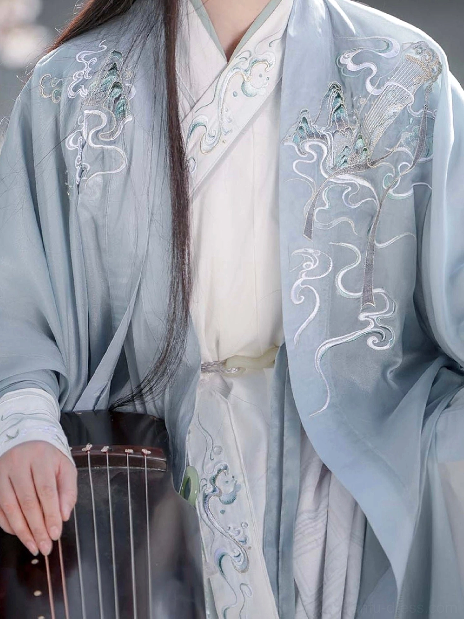 Close-up of xianxia hanfu cross collar with detailed phoenix and cloud embroidery beside a traditional guzheng