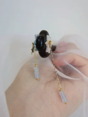 Back view of Xiaohan traditional Chinese hair stick held in hand, showing white snowflake pendant, dark wood pin, gold chains, and blue bead tassels