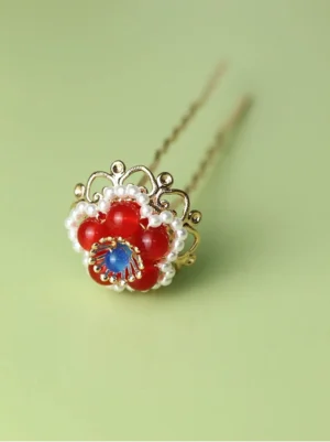 Red floral U-shaped Hanfu hair pin with blue center stone, pearl-like trim, and gold-tone decorative framework on a light green background