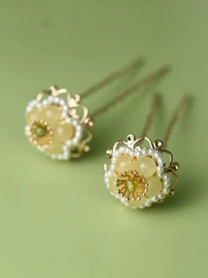 Pair of yellow floral U-shaped Hanfu hair pins with pale yellow petals, green center stones, and ornate gold-tone frames side view