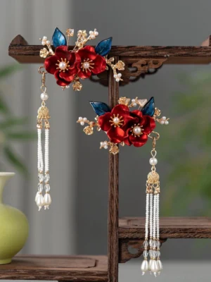 Pair of traditional Chinese wedding hairpins with red flowers blue accents gold-tone hardware and long pearl tassels displayed on a vintage wooden shelf