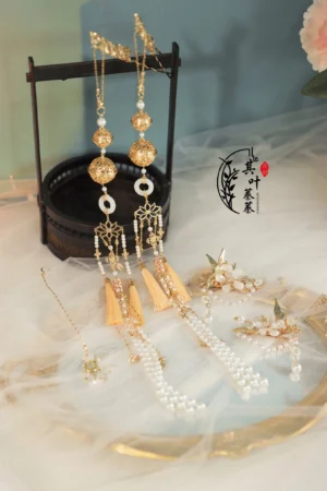 Complete Ye Xiwu Hanfu hair accessories set displayed on gauze with gold-tone hairpins, pearl chains, yellow tassels, white jade-inspired rings, and decorative headdress
