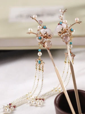 Pair of traditional Chinese hair sticks with golden flowering branches, milky white beads, turquoise-toned ornaments, and layered pearl tassels displayed beside a book