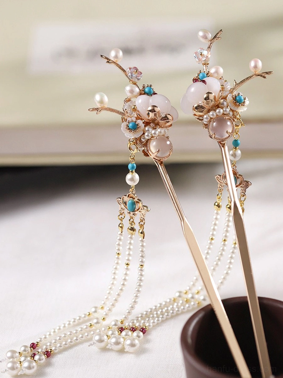 Pair of traditional Chinese hair sticks with golden flowering branches, milky white beads, turquoise-toned ornaments, and layered pearl tassels displayed beside a book