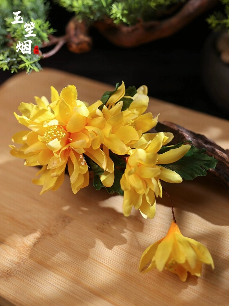 Close-up flat lay of yellow chrysanthemum hair accessories with layered petals and green leafy details on a wooden background