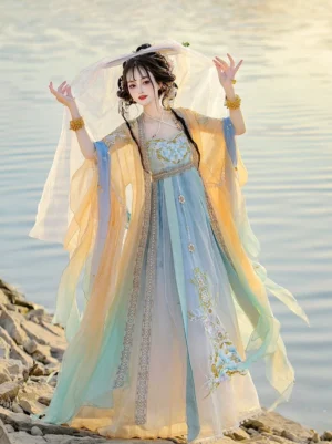 Yellow and cyan gradient Tang Dynasty Hanfu Heziqun dress set with floral embroidery, flowing sheer shawl, wide sleeves, and matching head veil photographed by a lakeside