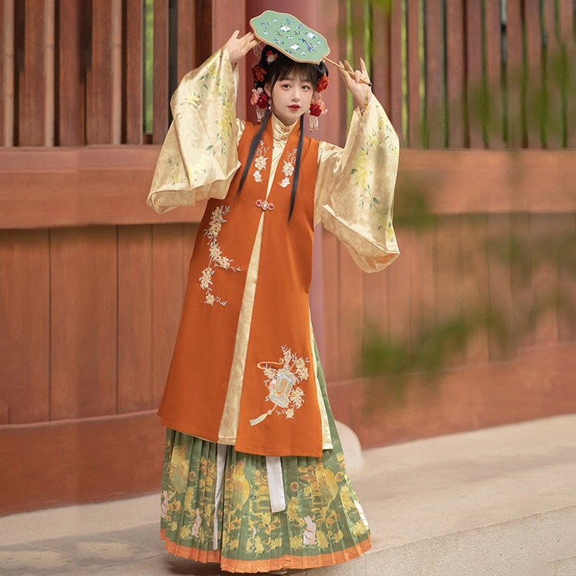 Full-body woman wearing the yellow Ming Dynasty hanfu set with cream beige bijia vest, salmon pink wide-sleeve robe, printed pleated skirt, and traditional hair accessories