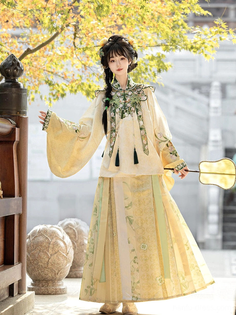 Cream yellow Ming style Hanfu set with embroidered cloud collar, floral horse-face mamian skirt and silk fan near a traditional Chinese wooden gate