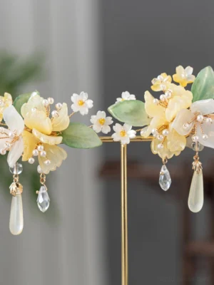 Close-up of yellow and white floral Hanfu hairpins and clips with green leaves faux pearls and dangling clear and milky glass charms on a golden display stand
