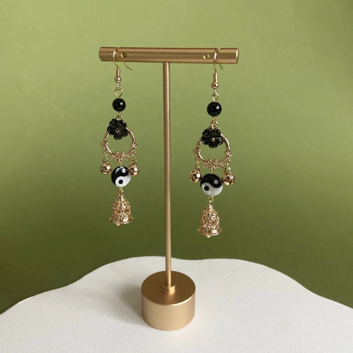 Yin Yang Tai Chi Chinese hook earrings displayed on jewelry stand with black beads floral details gold tone hardware and hollow bell drops