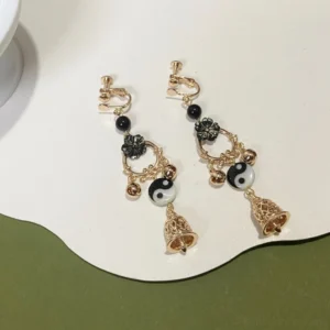 Yin Yang Tai Chi Hanfu comfort clip on dangle earrings with black flower ornaments gold tone charms and hollow bell pendants on white and olive green background