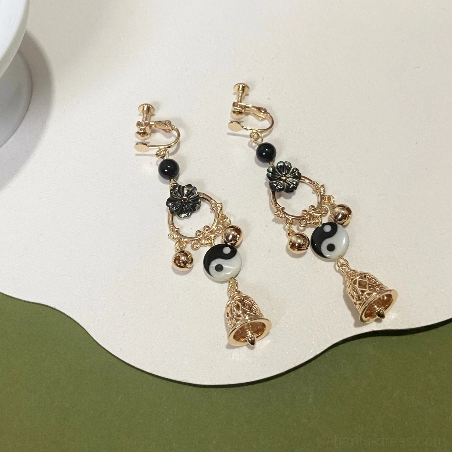 Yin Yang Tai Chi Hanfu comfort clip on dangle earrings with black flower ornaments gold tone charms and hollow bell pendants on white and olive green background