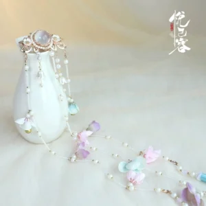 Yingliang traditional Chinese Hanfu back hair pin with gold tone floral centerpiece translucent gem pastel flower pendants pearl chains and silk tassels displayed on beige fabric