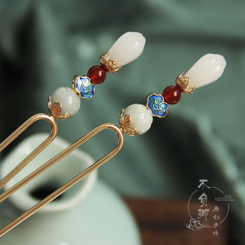 Yulan magnolia Chinese hair stick with double prongs, white jade blossom, red agate beads, blue cloisonne cloud ornament, and gold-tone shaft displayed beside a celadon tea set