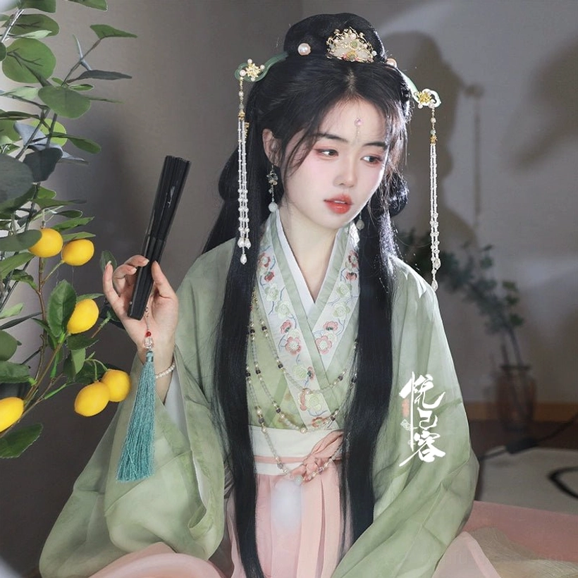 Three-quarter portrait of a woman wearing coordinated Yun Yan Ji Hanfu hair ornaments with gold, green, and white details while holding a black Chinese folding fan