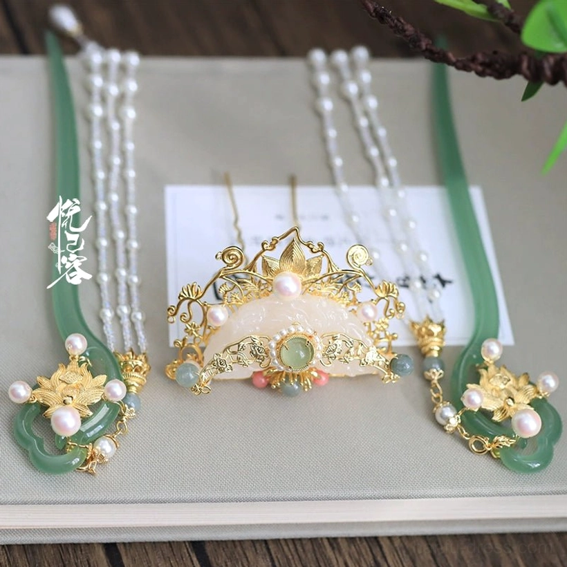 Yun Yan Ji Hanfu hair accessory pieces arranged on a vintage notebook and wooden table, including green jade-toned hairpins, pearl tassel chains, a crown, and gold decorations