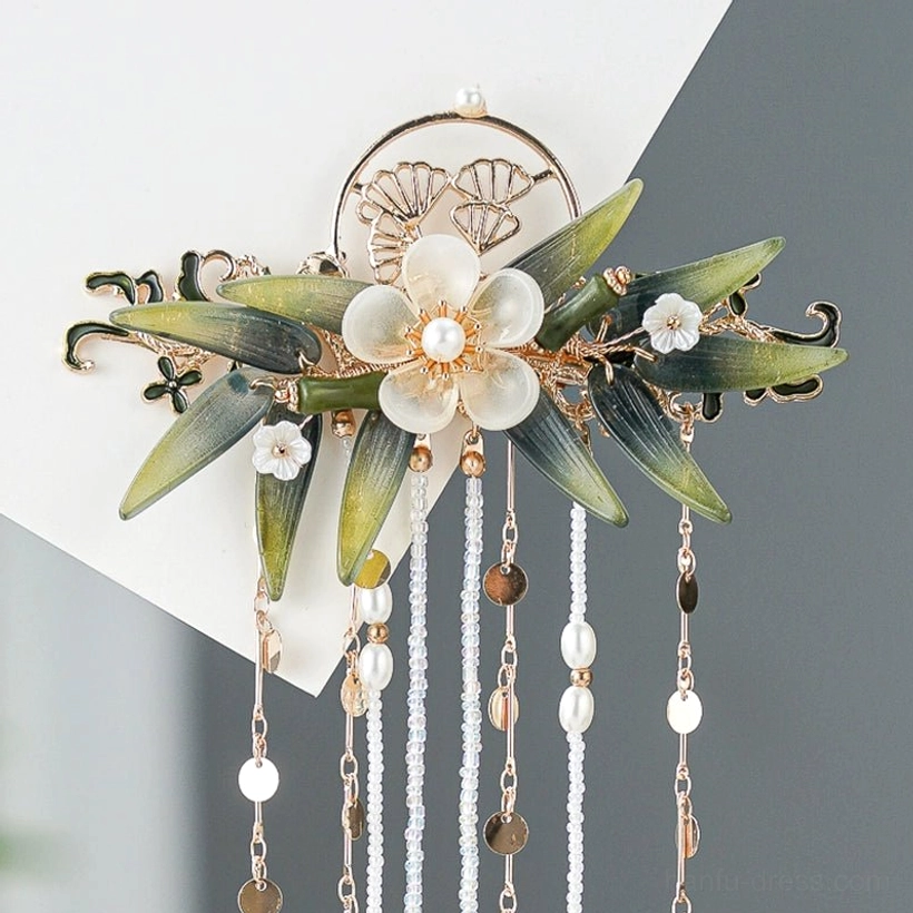 Close-up of the Zhuqin Chinese tassel hairpin showing pine cone-inspired metal ornament, small flowers, green bamboo leaves, beads, and multiple decorative tassel strands