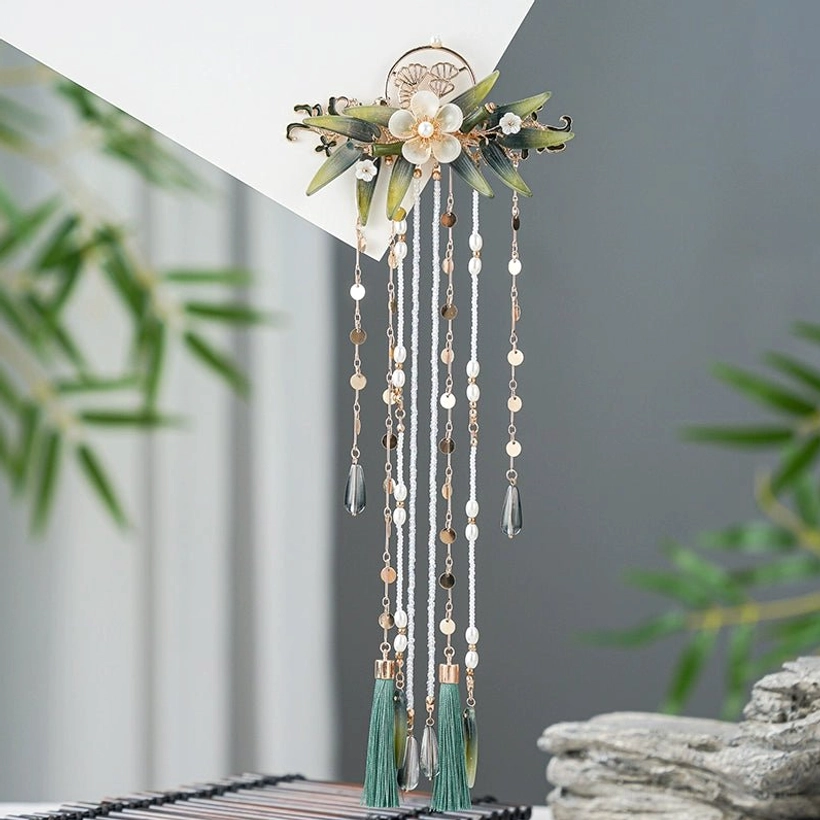 Oblique overhead view of the Zhuqin vintage Chinese hairpin with gold-toned base, floral decorations, green leaves, beaded tassels, and dark green pendant accents