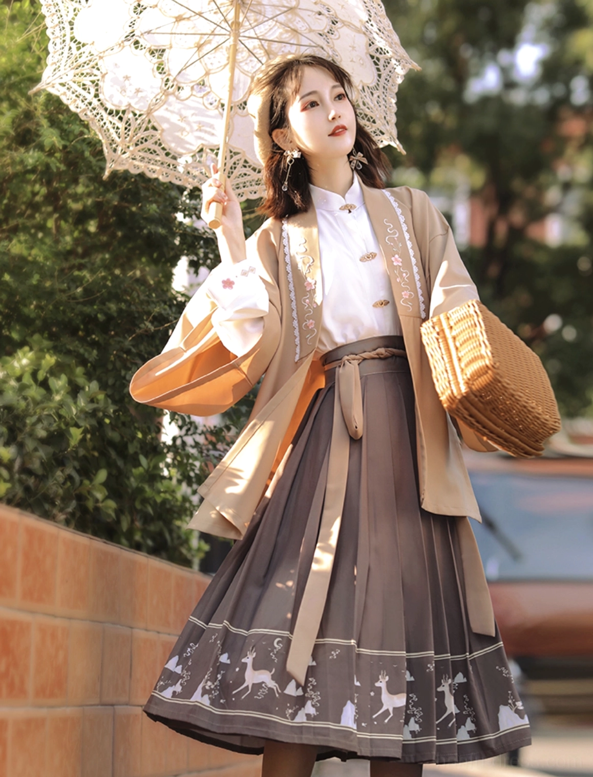 Full view of khaki Ming-inspired modern Hanfu three-piece set with floral embroidered cardigan, white stand-collar blouse, brown deer-print pleated skirt and woven basket bag
