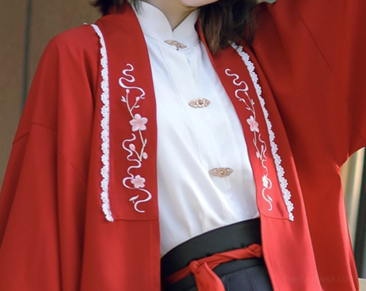 Close-up of red modern Hanfu cardigan showing pink floral vine embroidery, white trim, stand-collar blouse and brass Chinese frog-button details