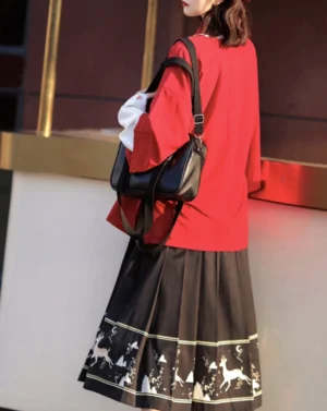 Back three-quarter view of red modern Hanfu embroidered cardigan outfit with black deer-print pleated skirt, green hem trim and black crossbody bag